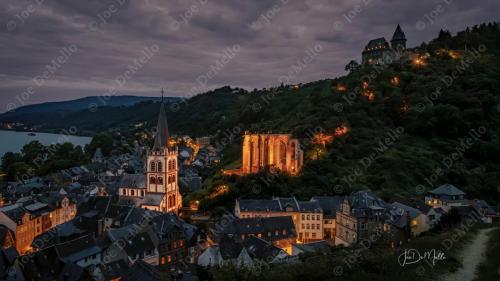 In the evening, Bacharach village transforms into a serene, picturesque setting along the Rhine River. As the sun sets behind the medieval castles and vineyards, the cobblestone streets glow under soft streetlights. The quaint houses and historic buildings exude charm, while the calm river reflects the fading light, creating a peaceful and romantic atmosphere perfect for evening strolls.