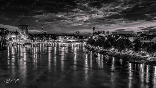 In black and white, Basel at night,A new perspective, a different light,The city's aura, now more dramatic and bold,A timeless moment, captured and told.